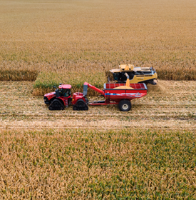 Yellow combine harvesting grain into a red trailer