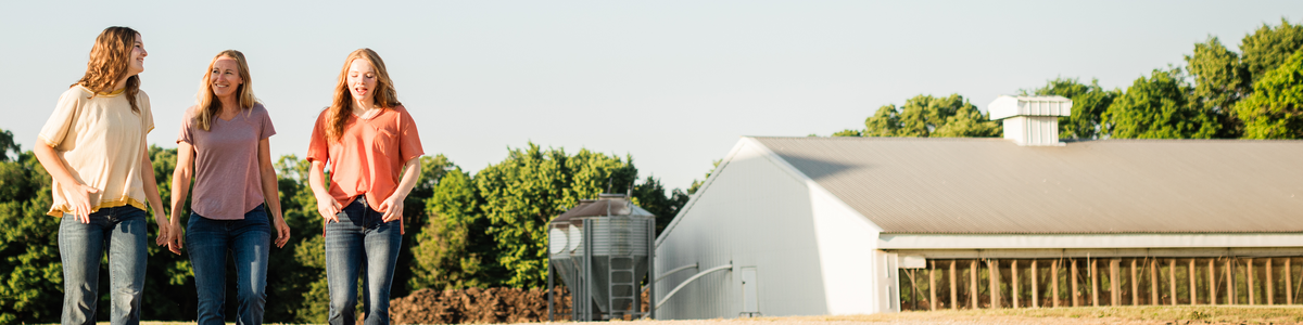 three women walking on a farm next to a hog barn
